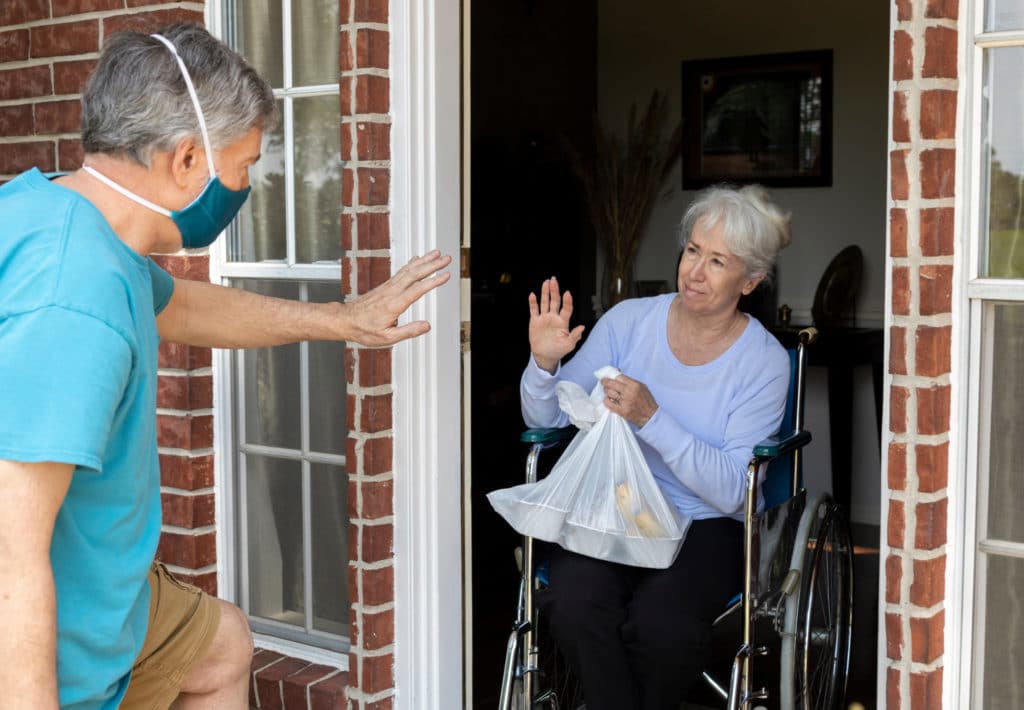 volunteer wearing a mask brings food to an elderly woman